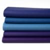 Stacked folded hides of smooth full-grain cow leather in blue and purple tones on a white background, part of the Milano Collection by Avetco