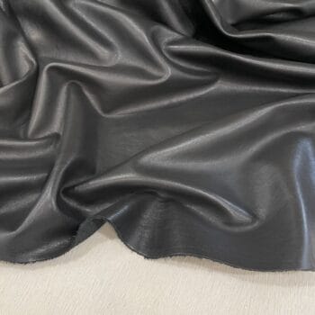 Dark gray, glossy leather fabric draped in soft folds and waves, showing texture and sheen on a light surface.