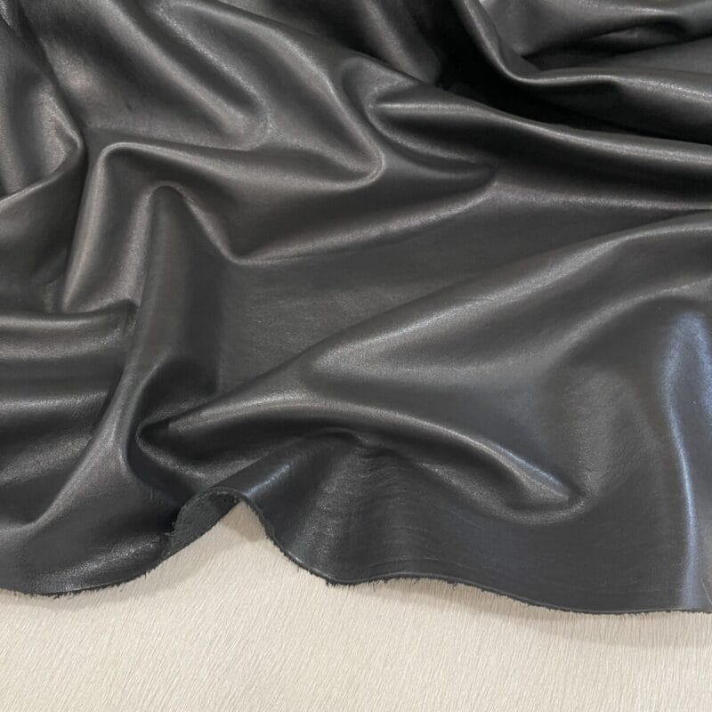 Lotto black cow leather Dark gray, glossy leather fabric draped in soft folds and waves, showing texture and sheen on a light surface.