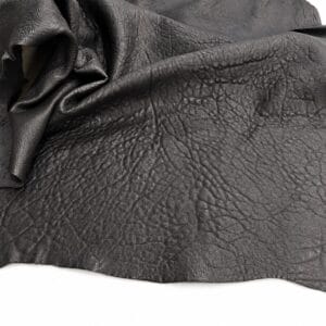 Close-up of black leather with prominent grain and folded texture, showing natural wrinkles and subtle sheen