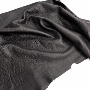 Close-up of black leather fabric showing grain and soft folds/creases on a white background.