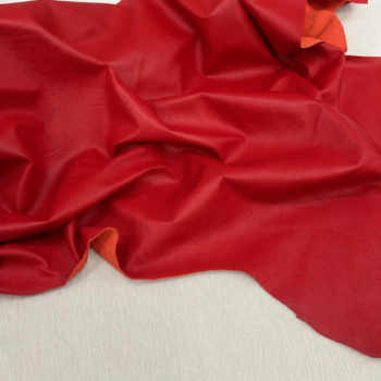 Red leather-like fabric laid out with soft folds and wrinkles on a light surface.