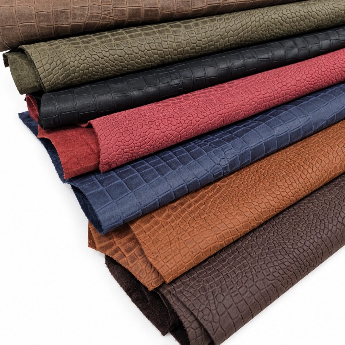 escape alligo cow leather crocco belly embossed Rolled leather fabric swatches in brown, tan, red, blue, and gray with a crocodile skin pattern laid in stacked layers
