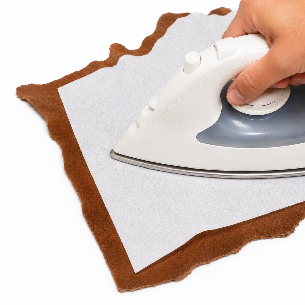 fabric Hand pressing a piece of gray fabric laid over brown felt with a white iron on top.