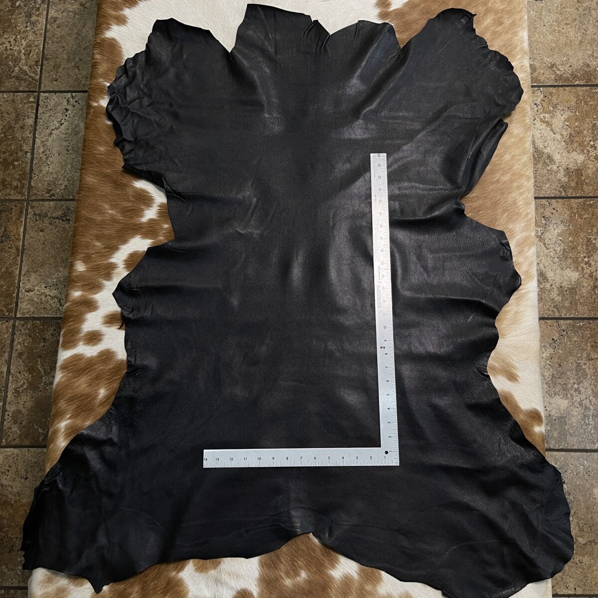 Black leather hide laid on a brown-and-white cowhide rug, with a metal ruler forming an L across it