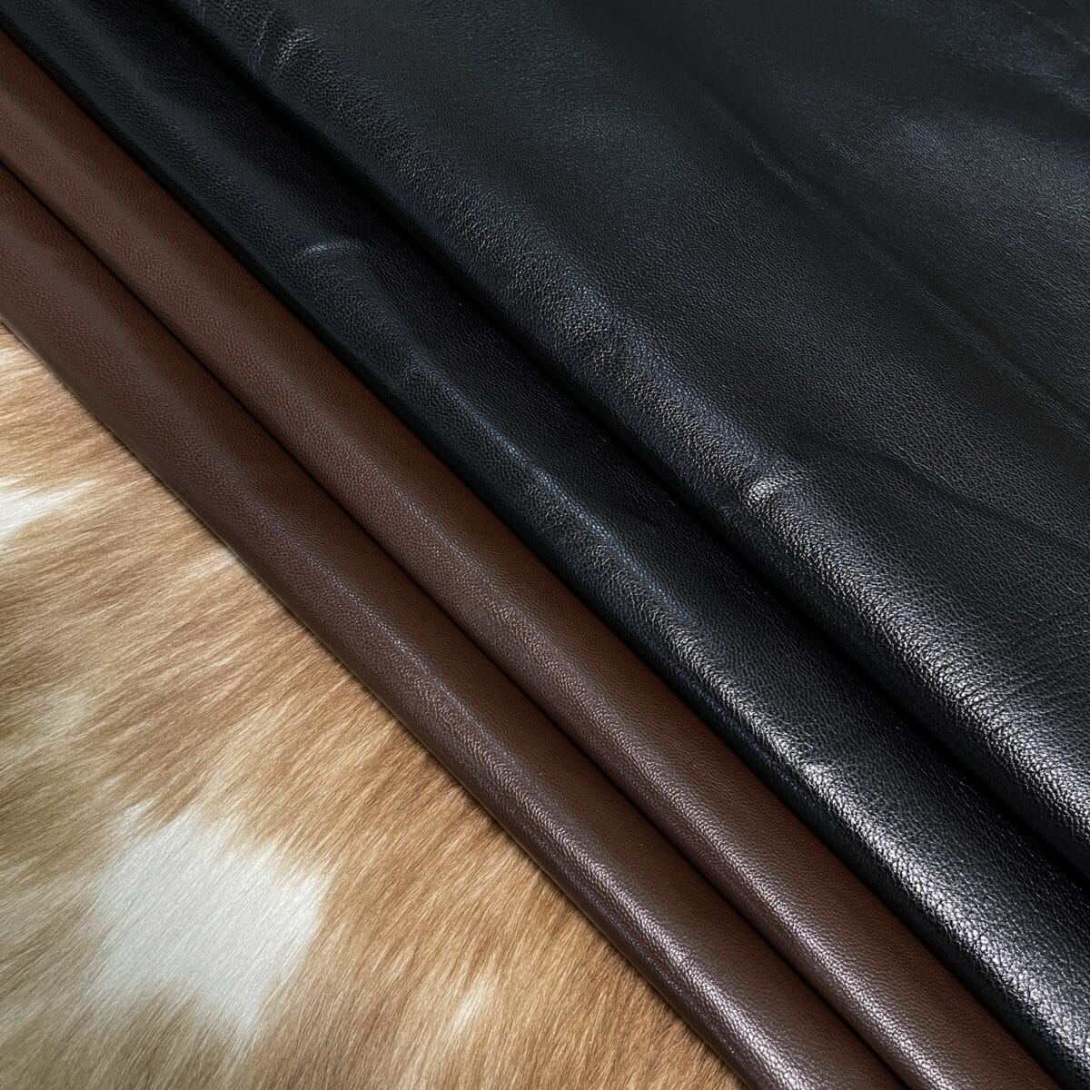 Leather swatches rolled into cylinders in brown and black, laid on a wooden surface