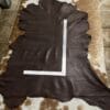 img_ Dark brown leather hide laid flat on a light cowhide rug, with a metal ruler arranged in an L-shape across it for measurement