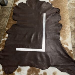 img_ Dark brown leather hide laid flat on a light cowhide rug, with a metal ruler arranged in an L-shape across it for measurement