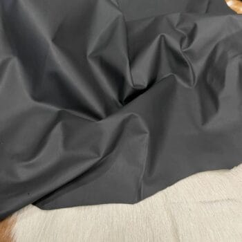 Crinkled black fabric laid on a light wooden surface, showing folds and shadows.