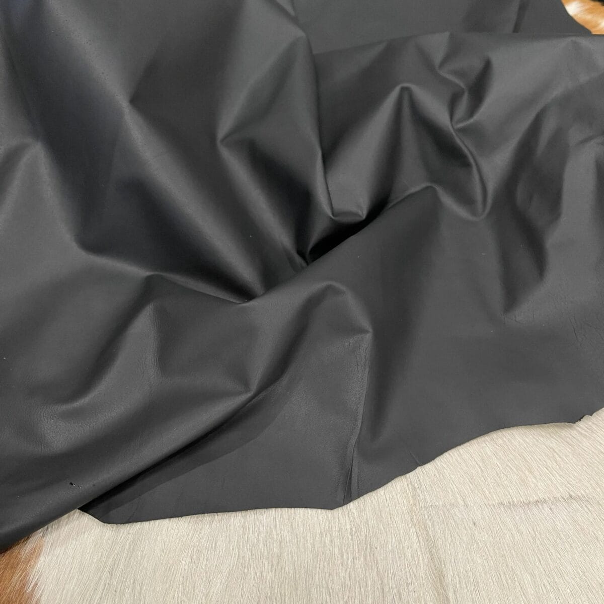 lambskin garment leather oz black Crinkled black fabric laid on a light wooden surface, showing folds and shadows.