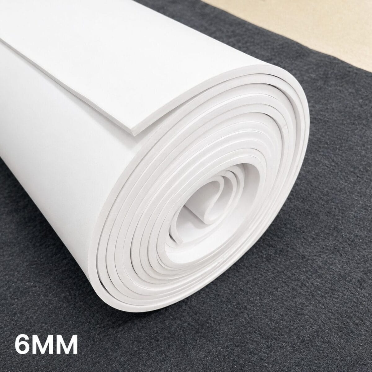 Rolled white foam board/panel, 6 mm thick, on a dark surface with one sheet partially unrolled showing its edge edge.