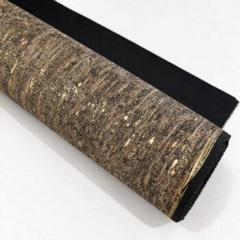Roll of cork-textured wallpaper or fabric with brown speckled pattern, partially unrolled on a white surface, showing black backing edge