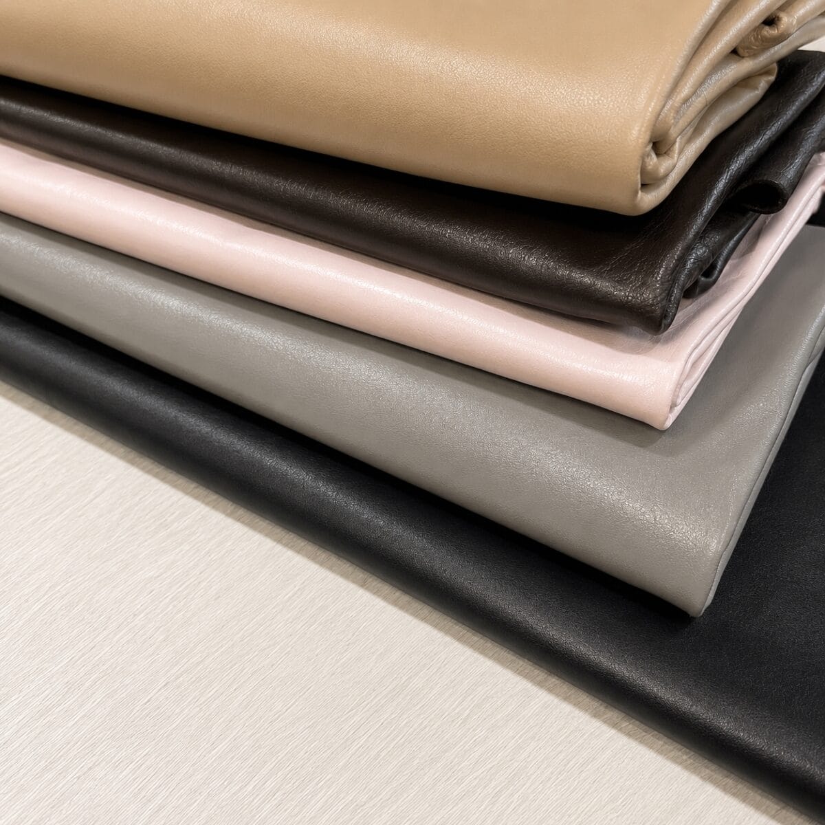 new mirlo Stack of folded leather or faux-leather fabrics in beige, tan, black, gray, and pale pink tones.