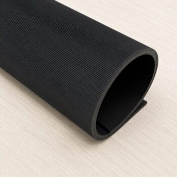 Black textured rubber mat rolled into a hollow cylinder on a light wooden surface