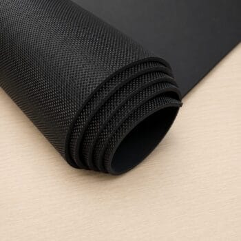 Rolled black textured yoga or exercise mat on a light wooden surface.