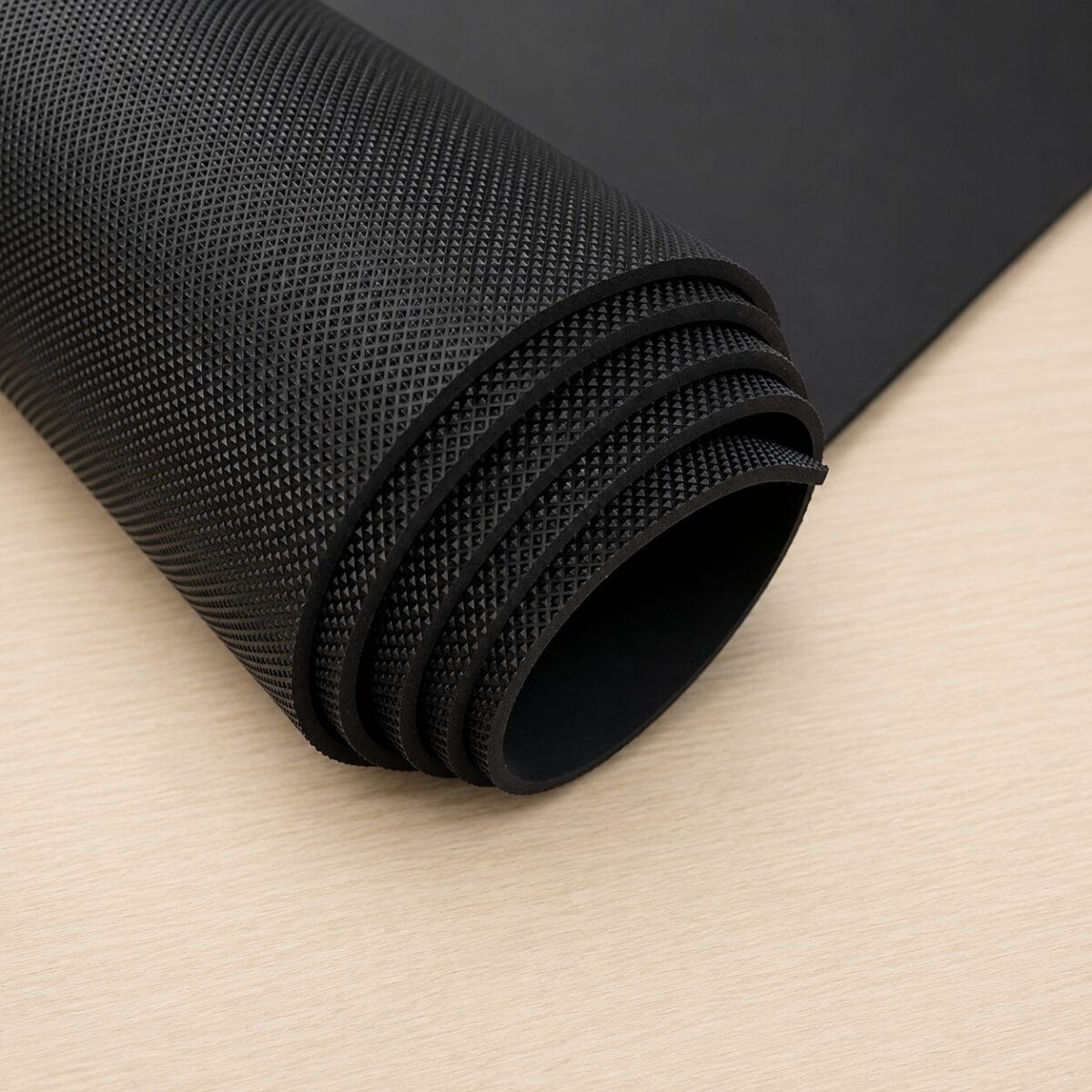 pyramid black large sheet Rolled black textured yoga or exercise mat on a light wooden surface.