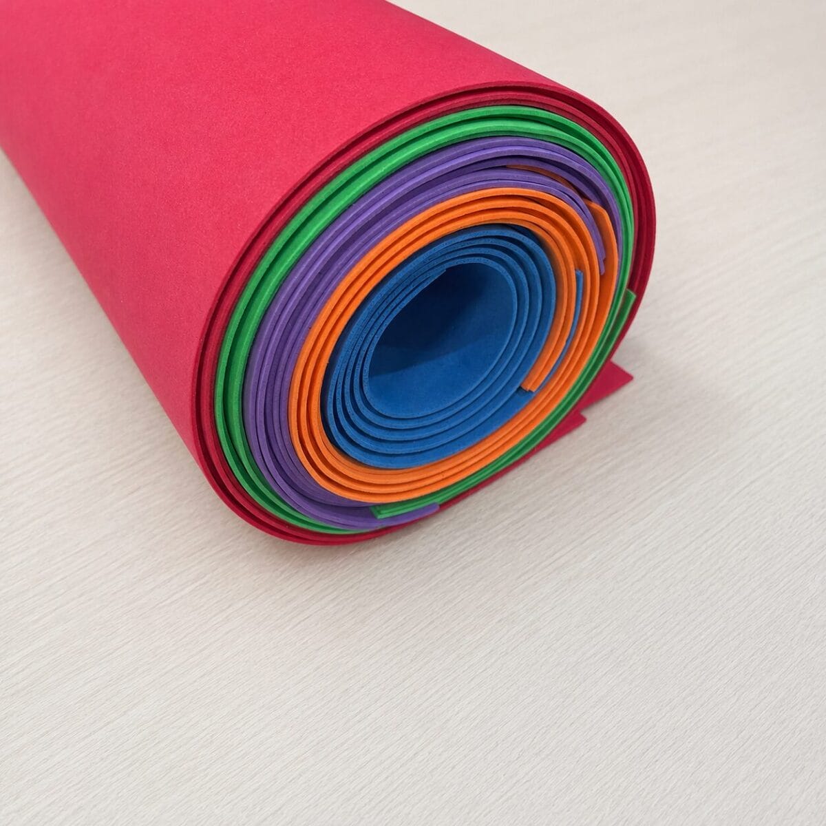rainbow mix sheets Rolled multicolor craft paper in a pink outer layer, forming a spiral stack for crafts.