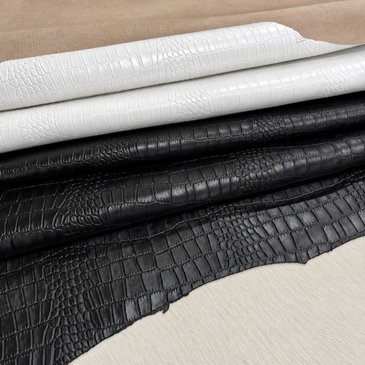 slalligo black and white Stacks of crocodile‑patterned leather rolls in beige, white, and black colors.