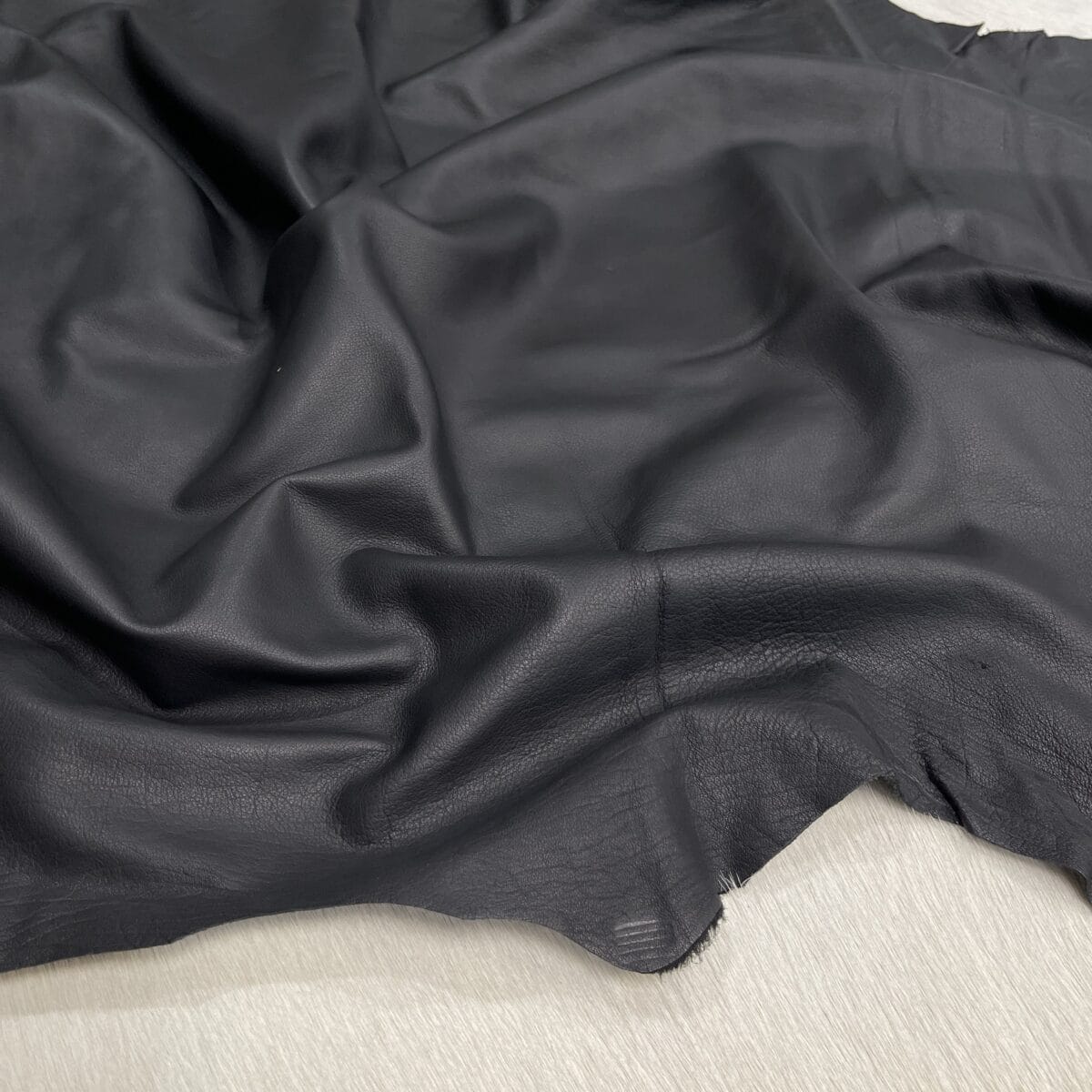 Dark gray leather fabric with soft folds spread over a light surface.