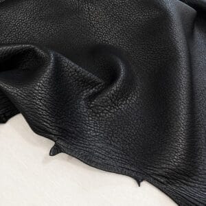 Close-up of black leather fabric with a pebbled texture draped over a light surface.