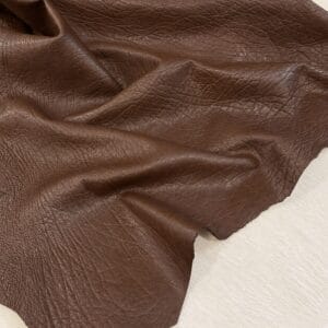 Brown leather fabric with visible grain and soft folds laid on a light wooden surface
