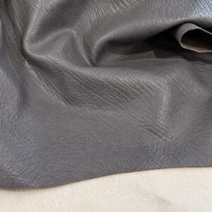 Close-up of gray leather fabric with visible grain resting on light fur surface.