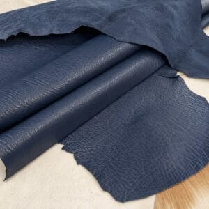 Blue leather hides laid flat with rolled sections, showing pebbled grain on a light surface.
