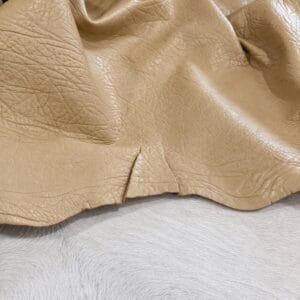 Tan leather fabric draped over light gray fur, showing grain and wrinkles in close-up.