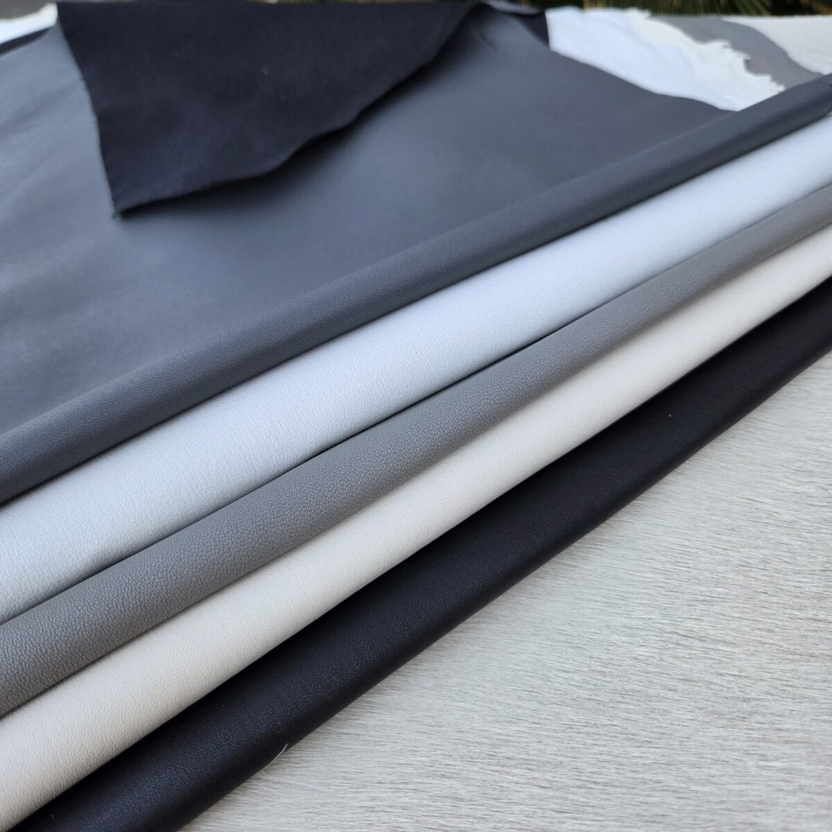 SL-115 stretch lamb Assorted SL-115 Stretch Lamb leather hides in black, light gray, gray, ivory, and navy blue displayed in a layered arrangement.