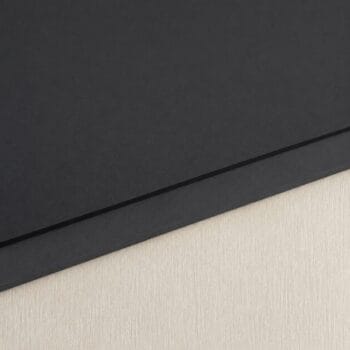 Close-up of a black notebook with a diagonal seam resting on a light wood surface.