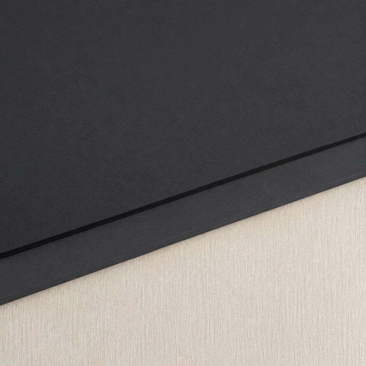 SP60A 5 & 10MM Close-up of a black notebook with a diagonal seam resting on a light wood surface.