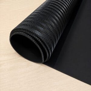 spchevron black large sheet Rolled black rubber anti-slip mat with a textured chevron pattern on a wooden desk surface.