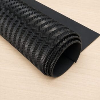 Rolled black textured mat with a chevron pattern on a light wooden surface, ready to use or unroll.