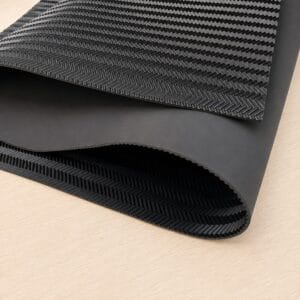 spchevron black large sheet Rolled black rubber mat with a textured herringbone pattern on a light wood surface, partially unrolled to show its underside edge