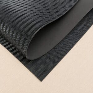spchevron black large sheet Close-up of rolled black rubber mat with a chevron/herringbone texture laid on a light wood surface